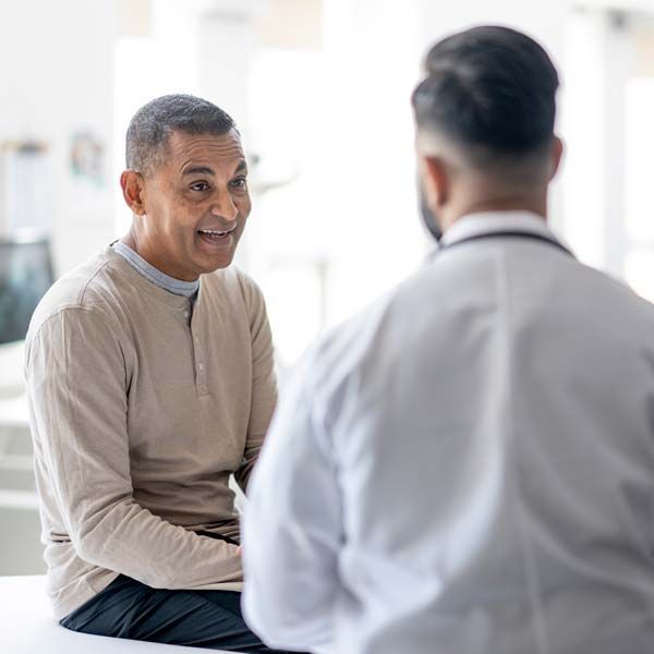 Two people talking in a bright medical office, one seated and smiling during a consultation