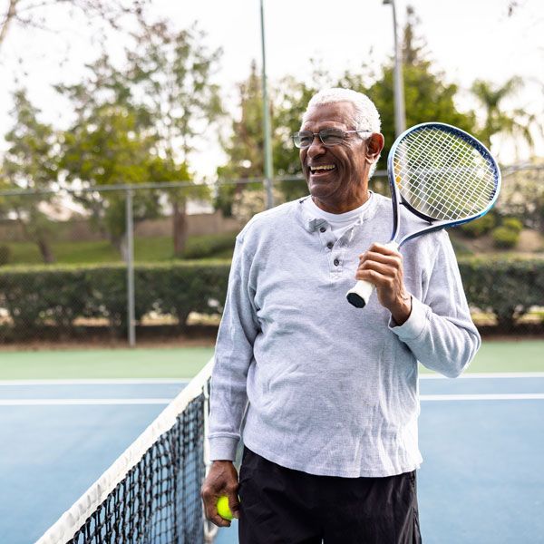 Smiling tennis player holding racket and ball on an outdoor court