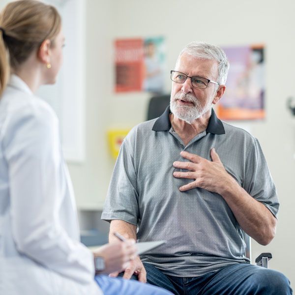 Patient speaking with clinician in a bright clinic, hand on chest during consultation.