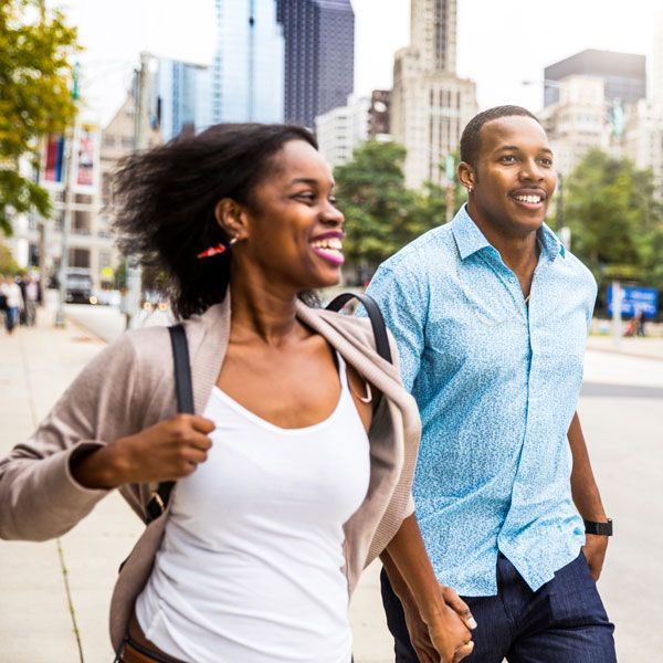 Two smiling people walking hand in hand on a city street with tall buildings in the background