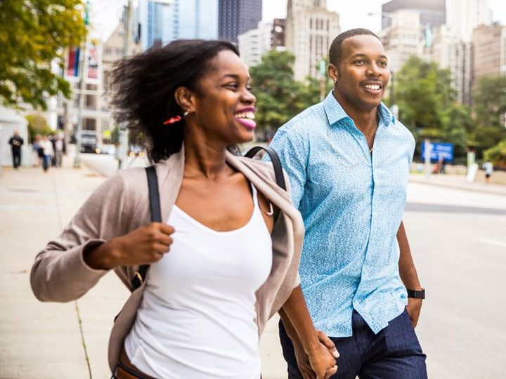 Two smiling people walking hand in hand on a city sidewalk