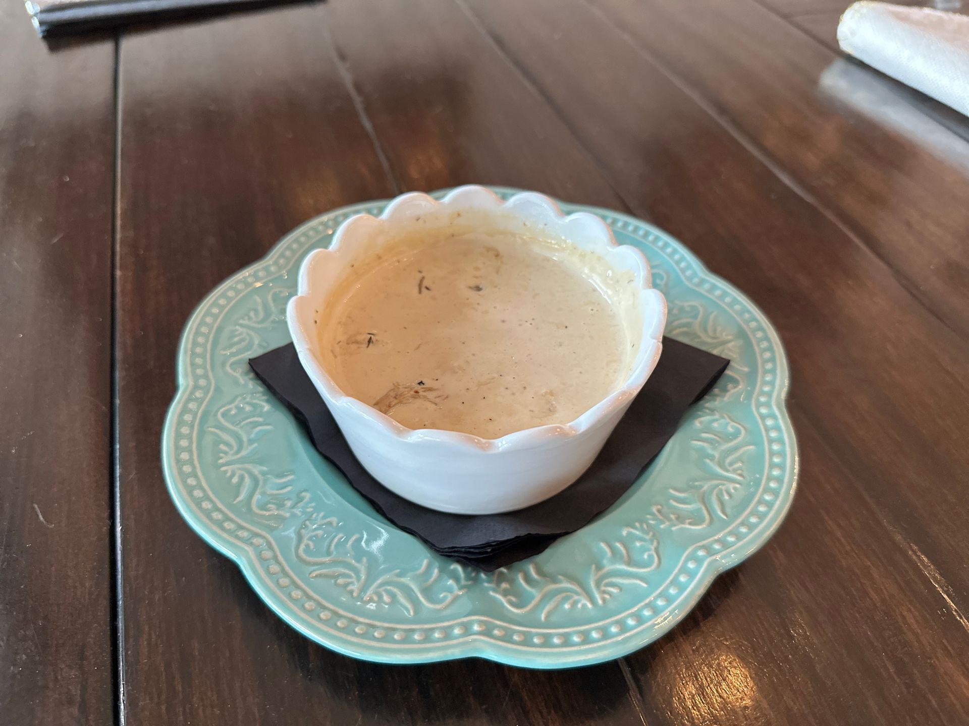 A bowl of soup is on a blue plate on a wooden table.