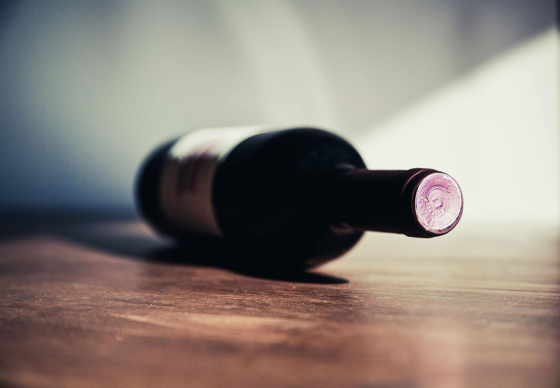 A bottle of wine is laying on its side on a wooden table.