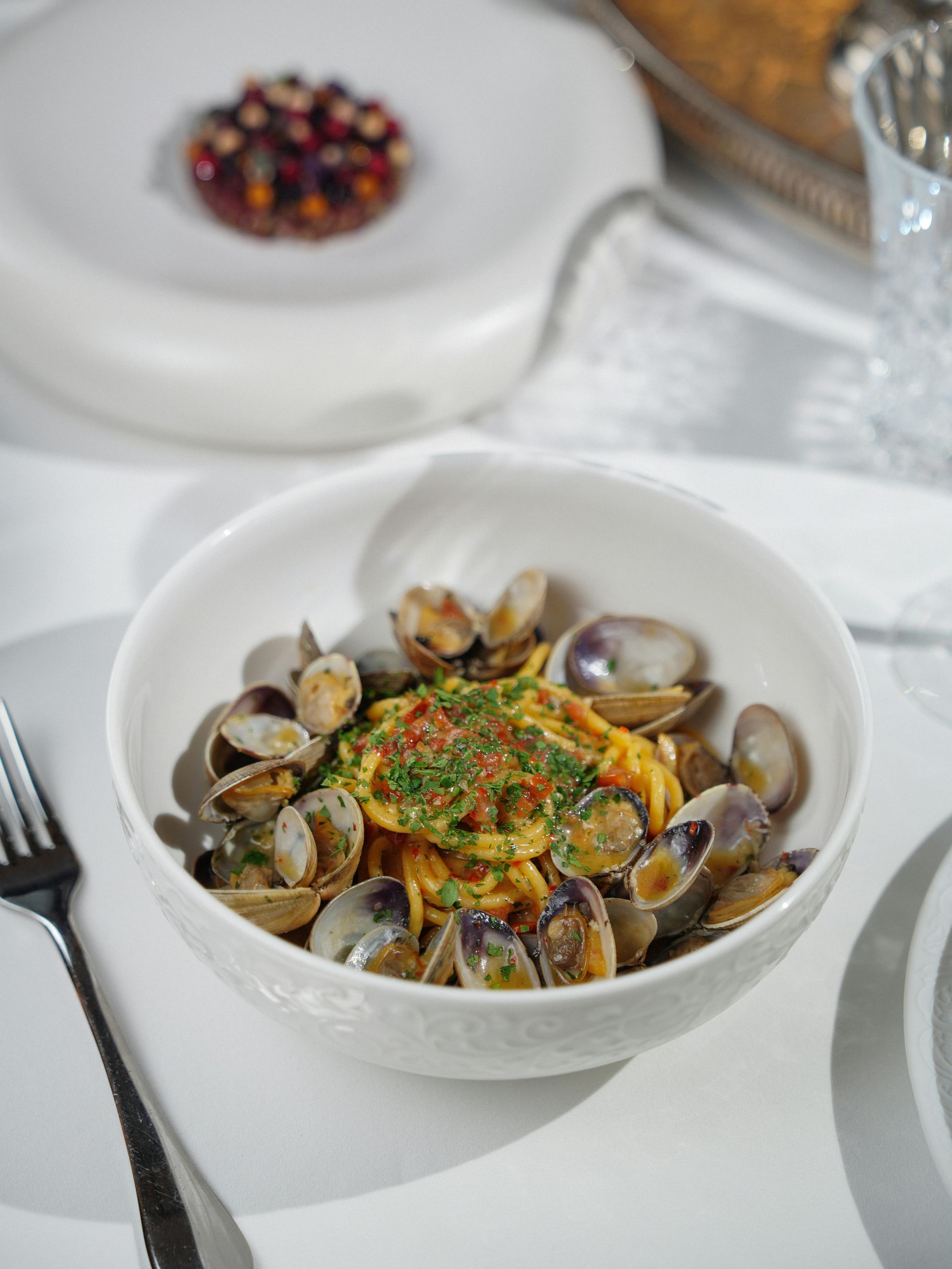 A bowl of clams and noodles on a table with a fork.