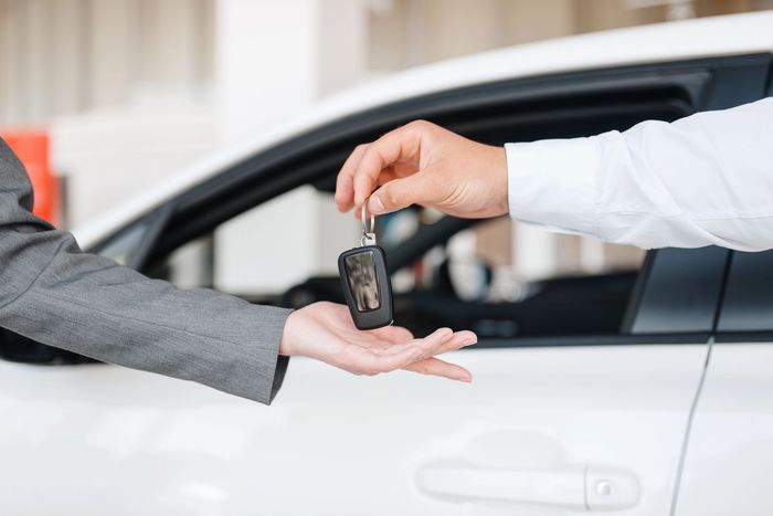 Persona che consegna le chiavi dell'auto a un'altra persona vicino a un'auto bianca.