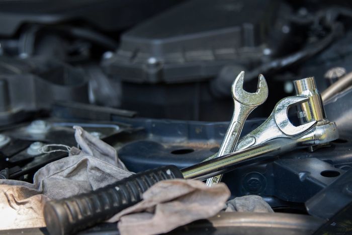 Persona che utilizza un computer portatile per diagnosticare il motore di un'auto, all'aperto.