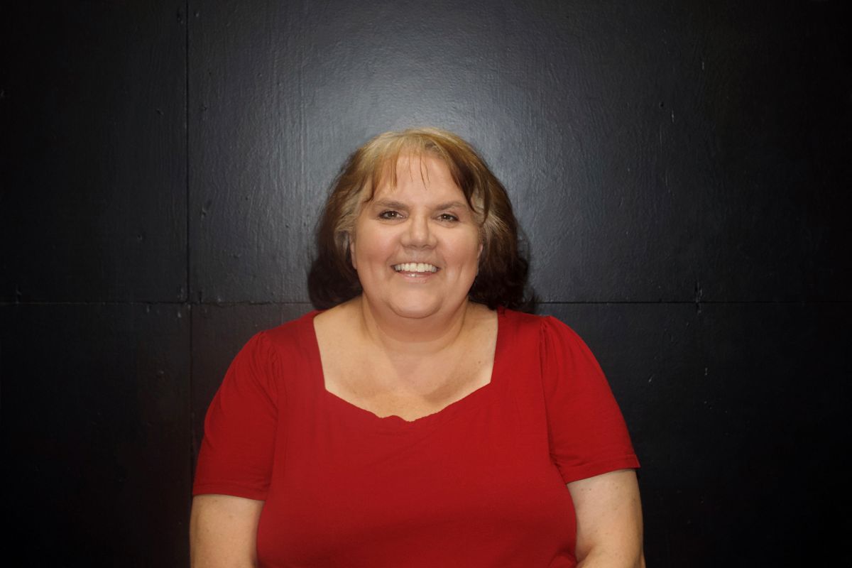 Woman in blue shirt smiles in a dimly lit basement.