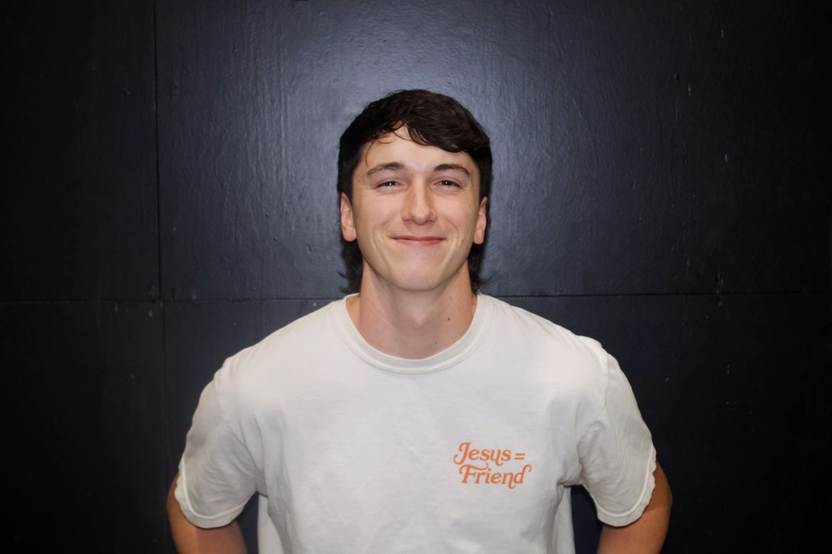 Man in gray Champion shirt smiles in a gym setting.