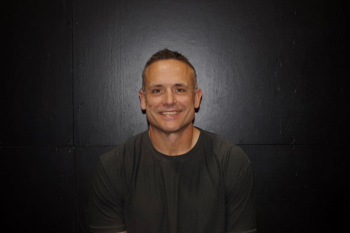 Man in a Dallas Cowboys jersey smiles in a basement gym with weights.