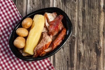 Sartén negra con patatas, mazorcas de maíz y carne a la parrilla sobre una mesa rústica.
