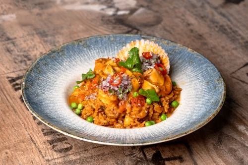 Arroz colorido cubierto con verduras y hierbas en un plato azul sobre una mesa de madera.