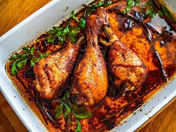 Muslos de pollo al horno en una fuente blanca con salsa oscura y hierbas sobre una mesa de madera.
