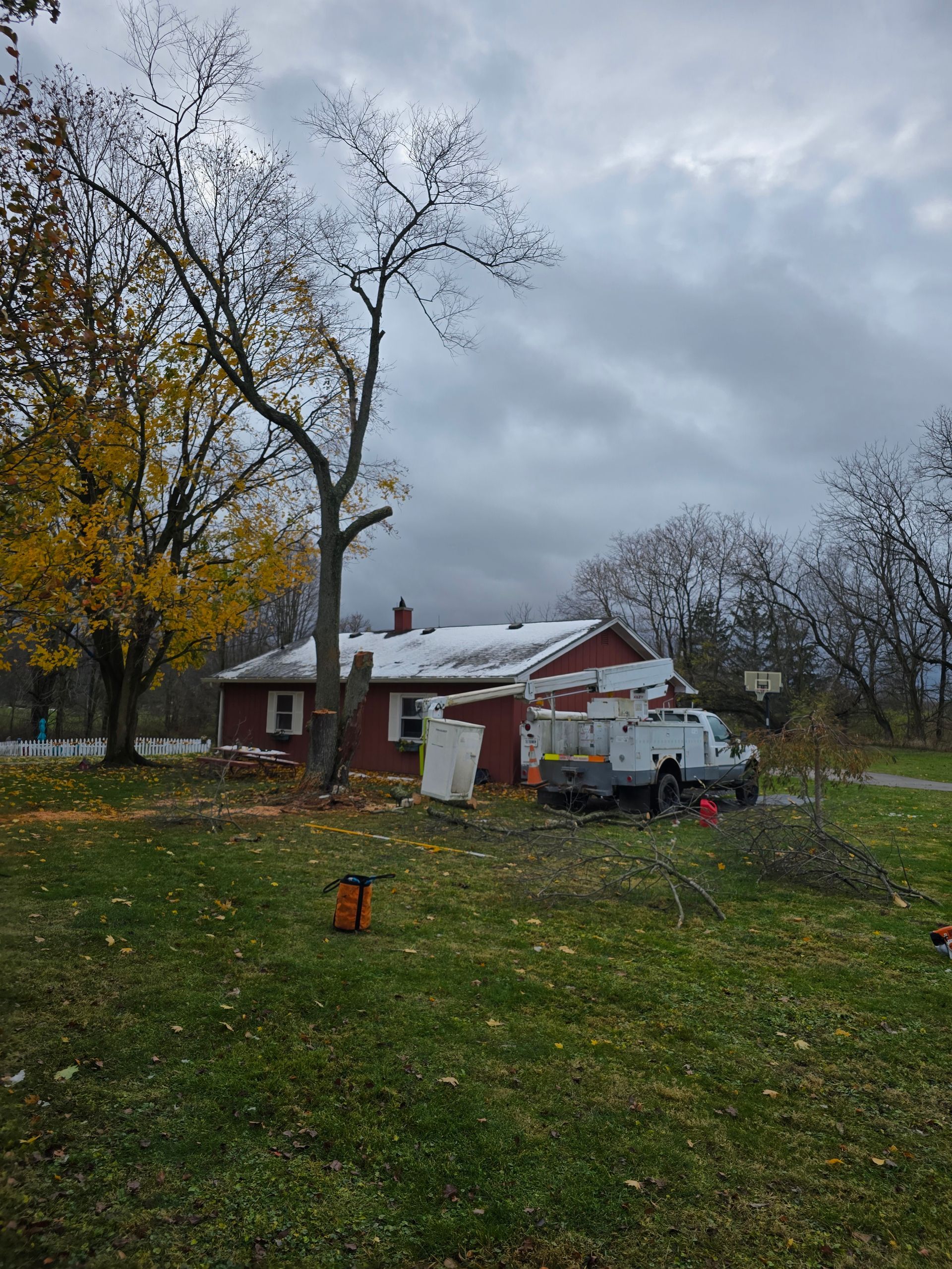 A utility truck parked next to a small red house with a snow-dusted roof, near a tree being trimmed on an overcast day.
