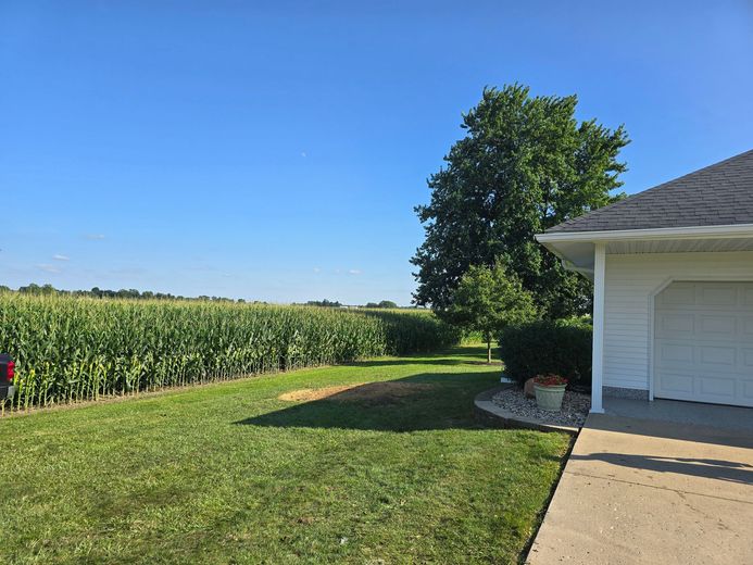 A white garage exterior beside a lush green cornfield under a clear, bright blue sky.