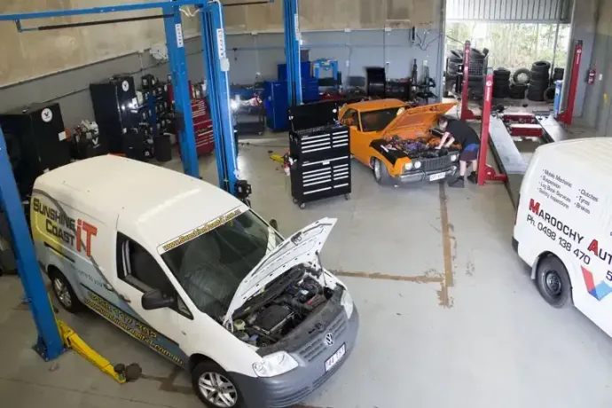 A White Van with The Hood Open Is Sitting on A Lift in A Mechanic Workshop — Maroochy Automotive in Matoochydore, QLD