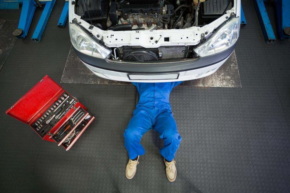 Mechanic in Blue Coveralls Working Under a Car on a Lift — Maroochy Automotive in Kunda Park, QLD