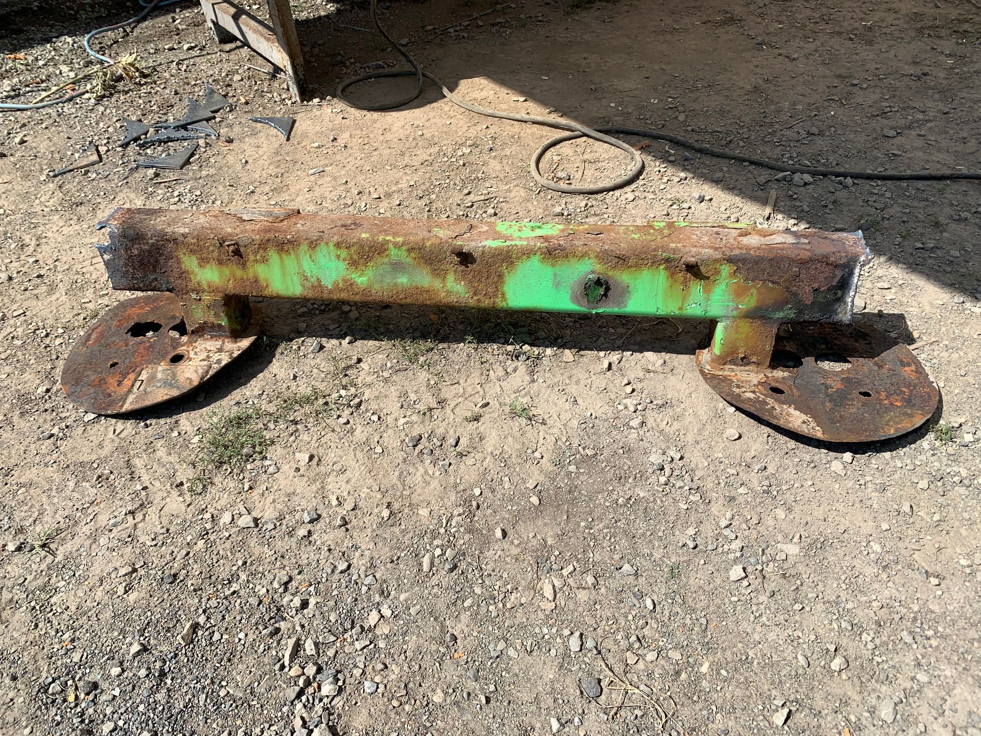 Outil agricole en métal vert rouillé sur du gravier.