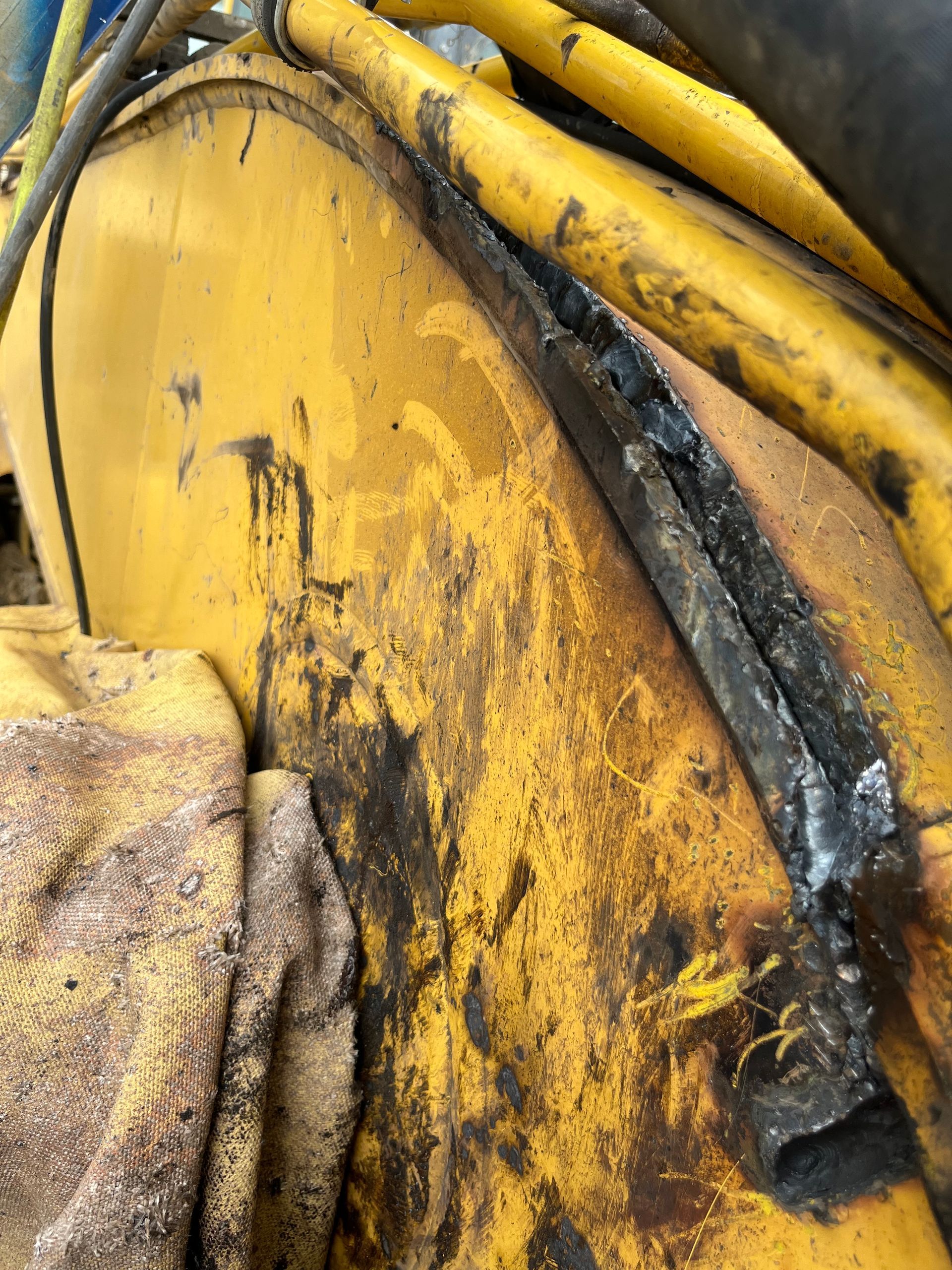 Machines jaunes, probablement du matériel de construction, présentant des signes d'usure, avec des taches sombres et une partie endommagée.