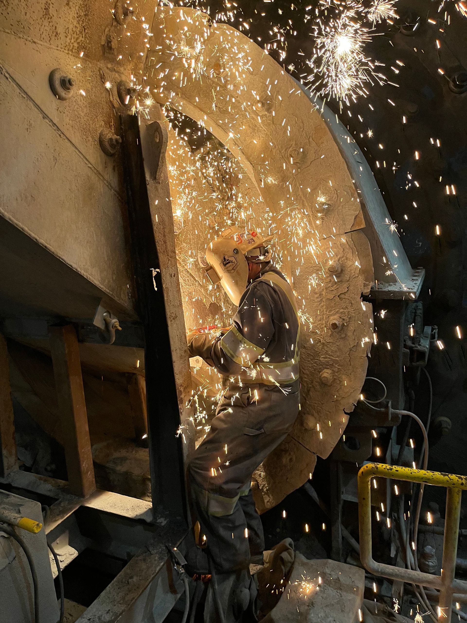 Un ouvrier découpe du métal, des étincelles jaillissent dans une usine de fabrication métallique.