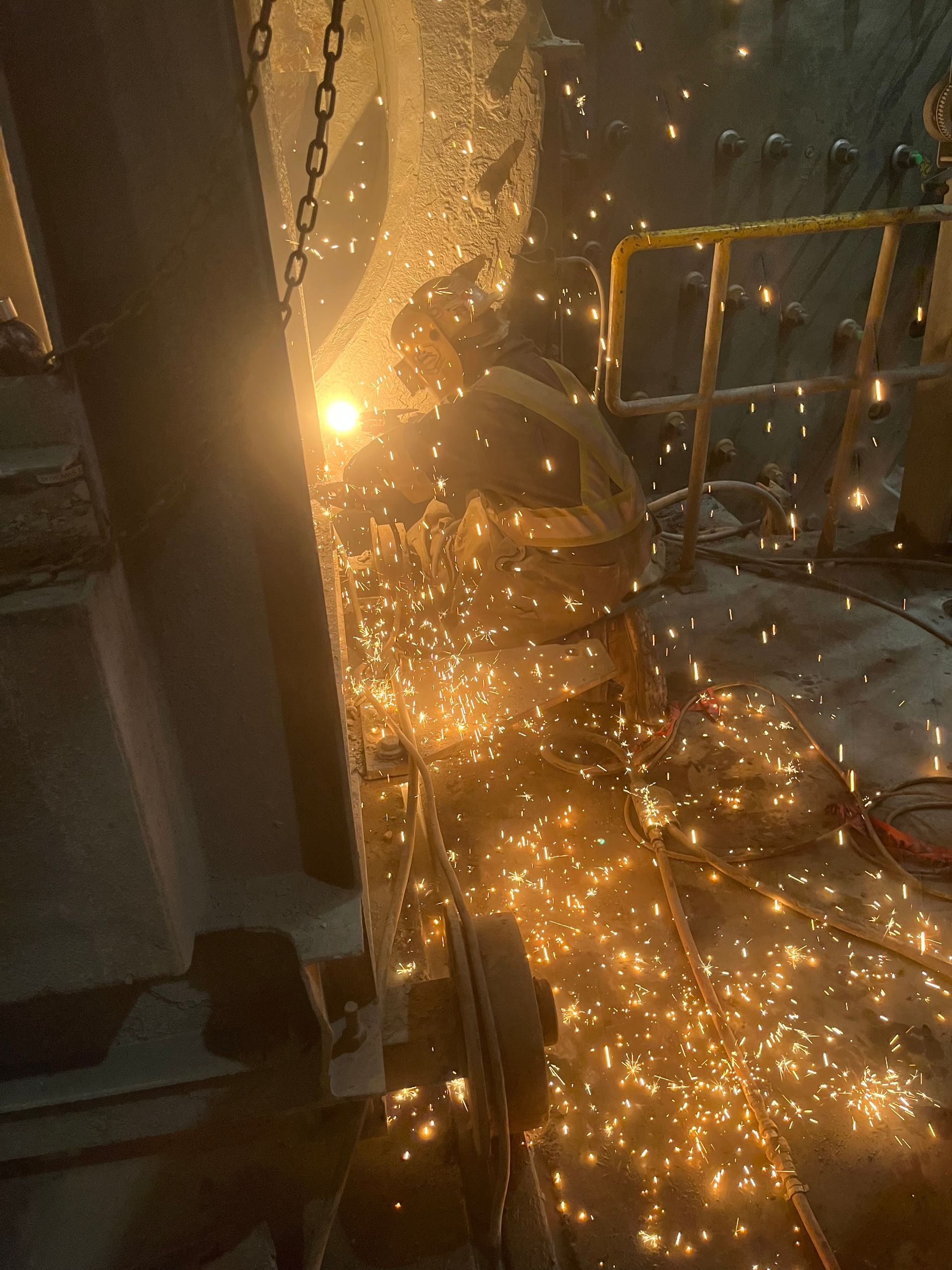 Des étincelles jaillissent des travaux de soudure sur la structure métallique, des lumières jaunes et orange illuminant le décor.