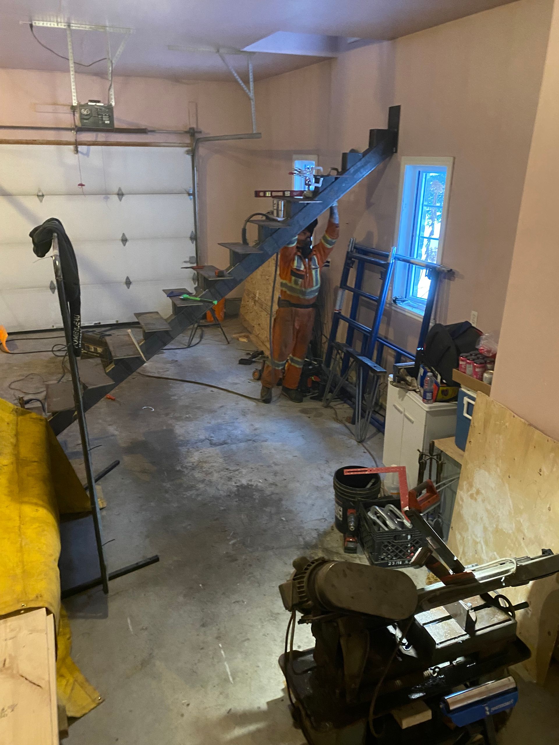 L'intérieur d'un garage encombré, avec une porte de garage fermée, un escalier, des outils et du matériel.