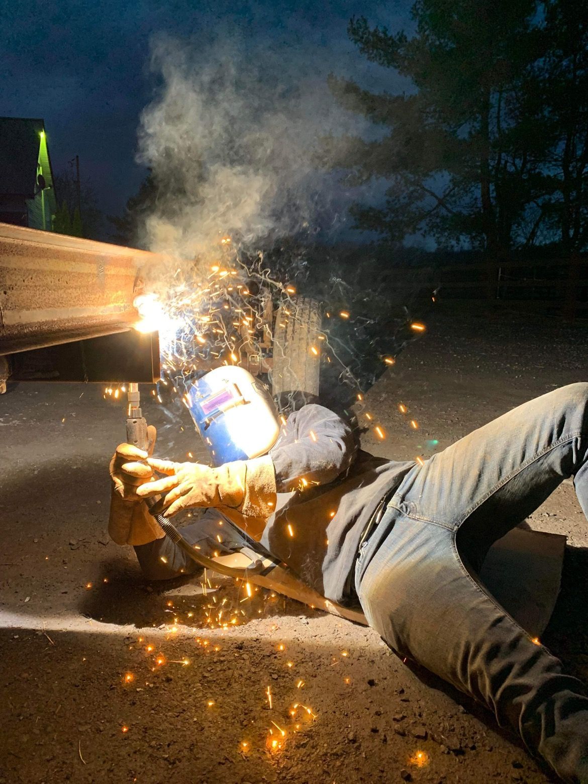 Une personne soude du métal en extérieur la nuit, des étincelles volent.