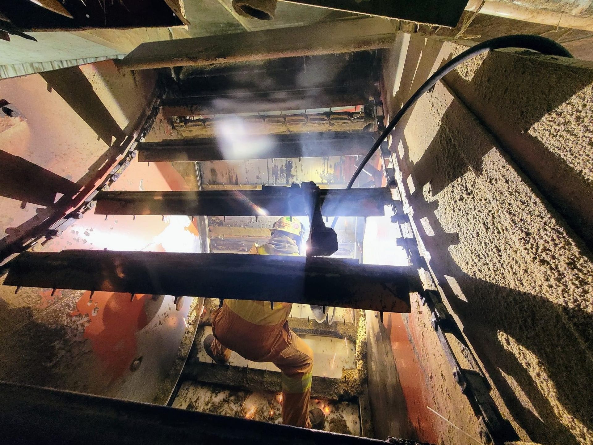 Soudeur travaillant dans un espace confiné à l'aide d'un chalumeau, des étincelles volent, portant un équipement de protection.