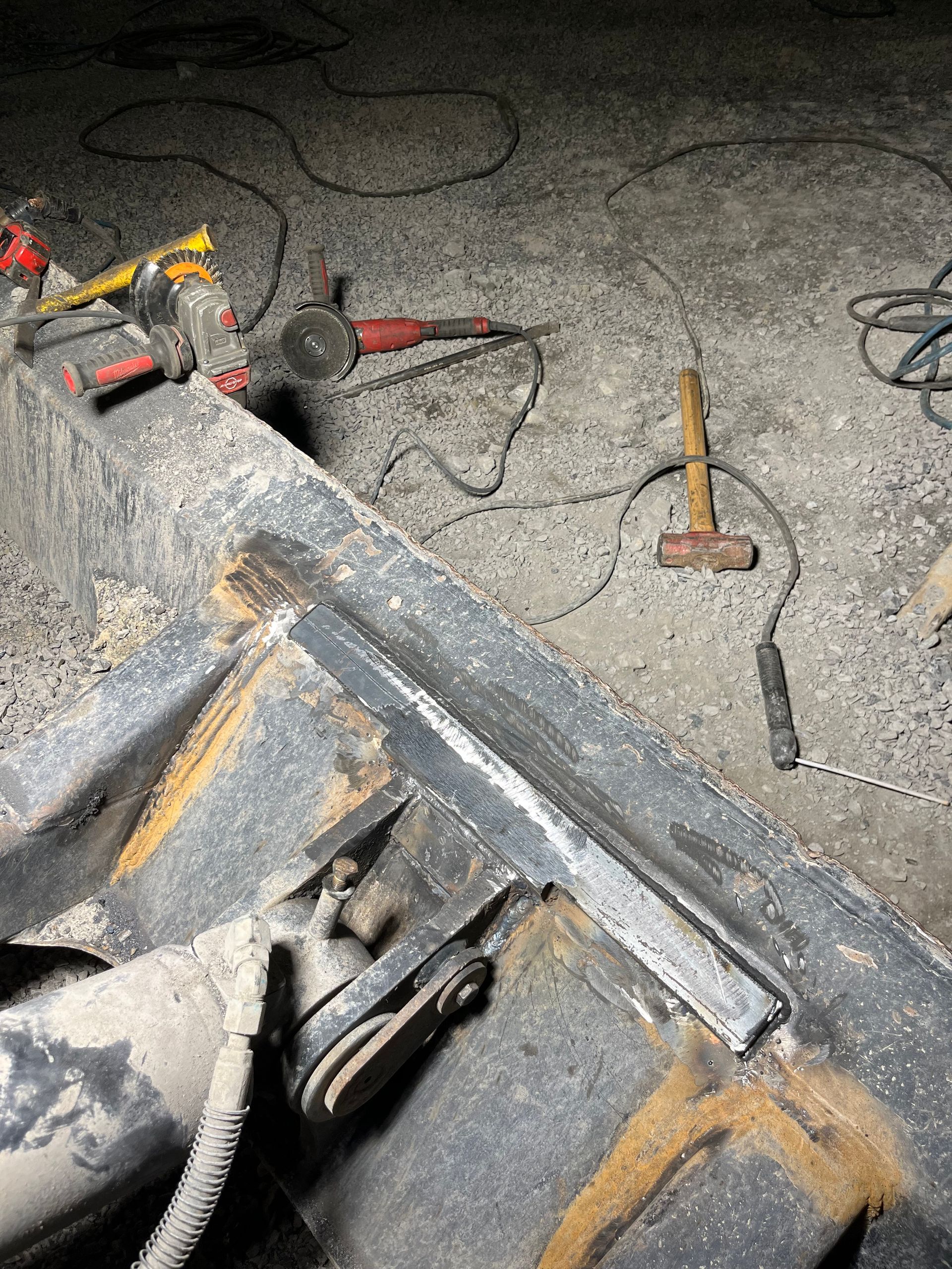 Réparation par soudure sur engin lourd. Métal gris avec cordon de soudure, outils éparpillés sur un sol en béton.