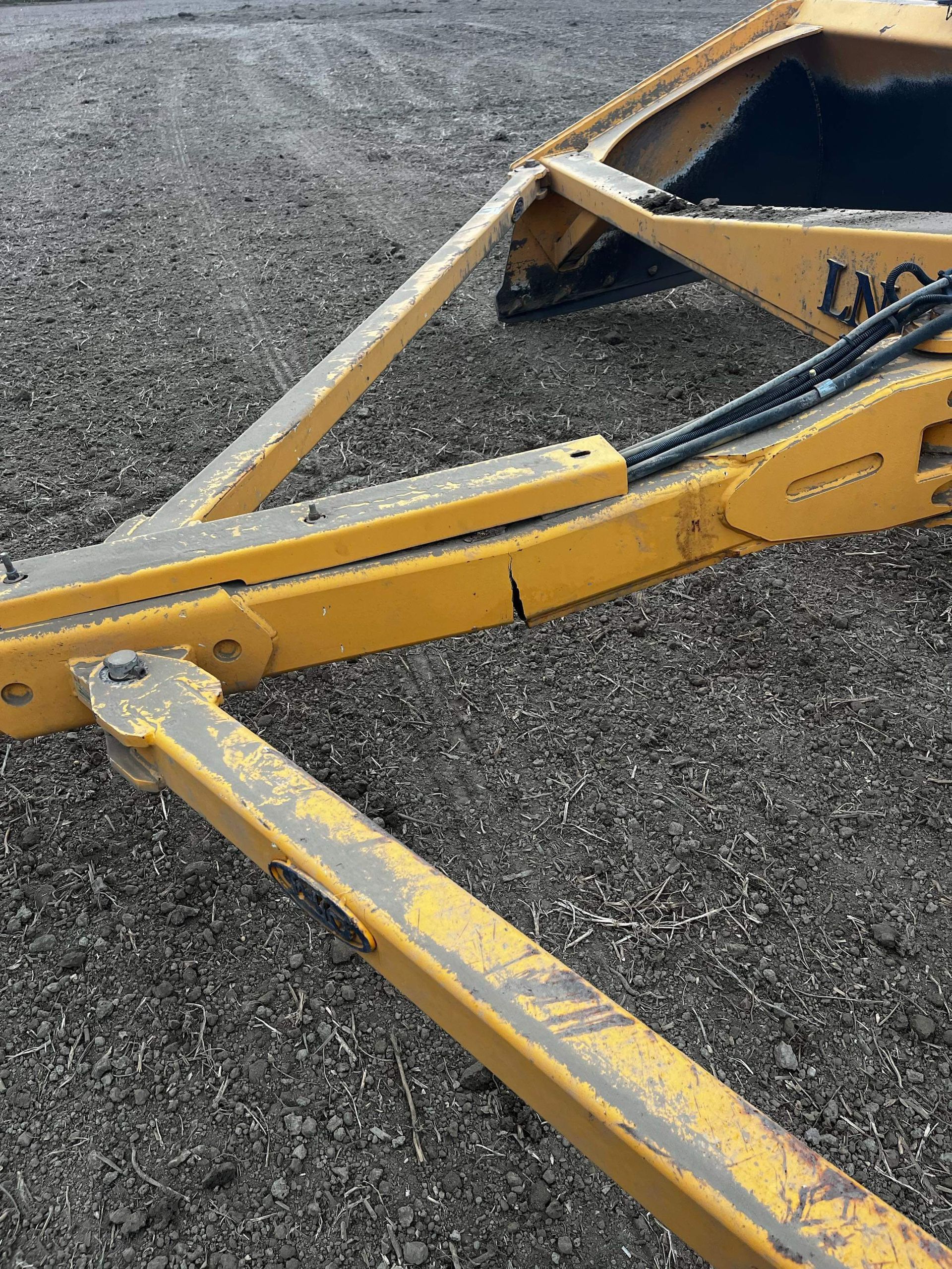 Outil agricole jaune muni d'une lame, sur une surface sombre.