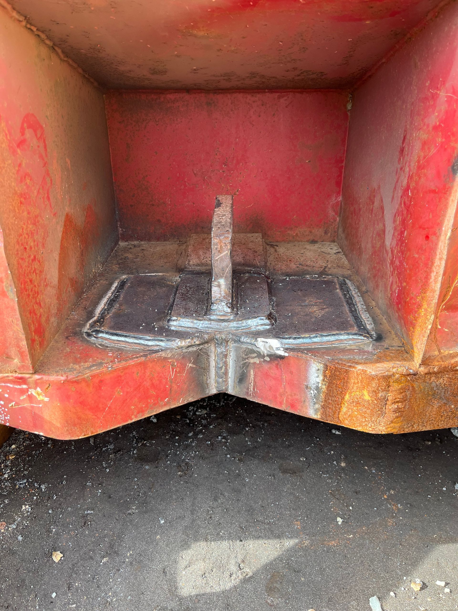 Intérieur d'une benne à ordures en métal rouge avec plaque et support en métal soudé.