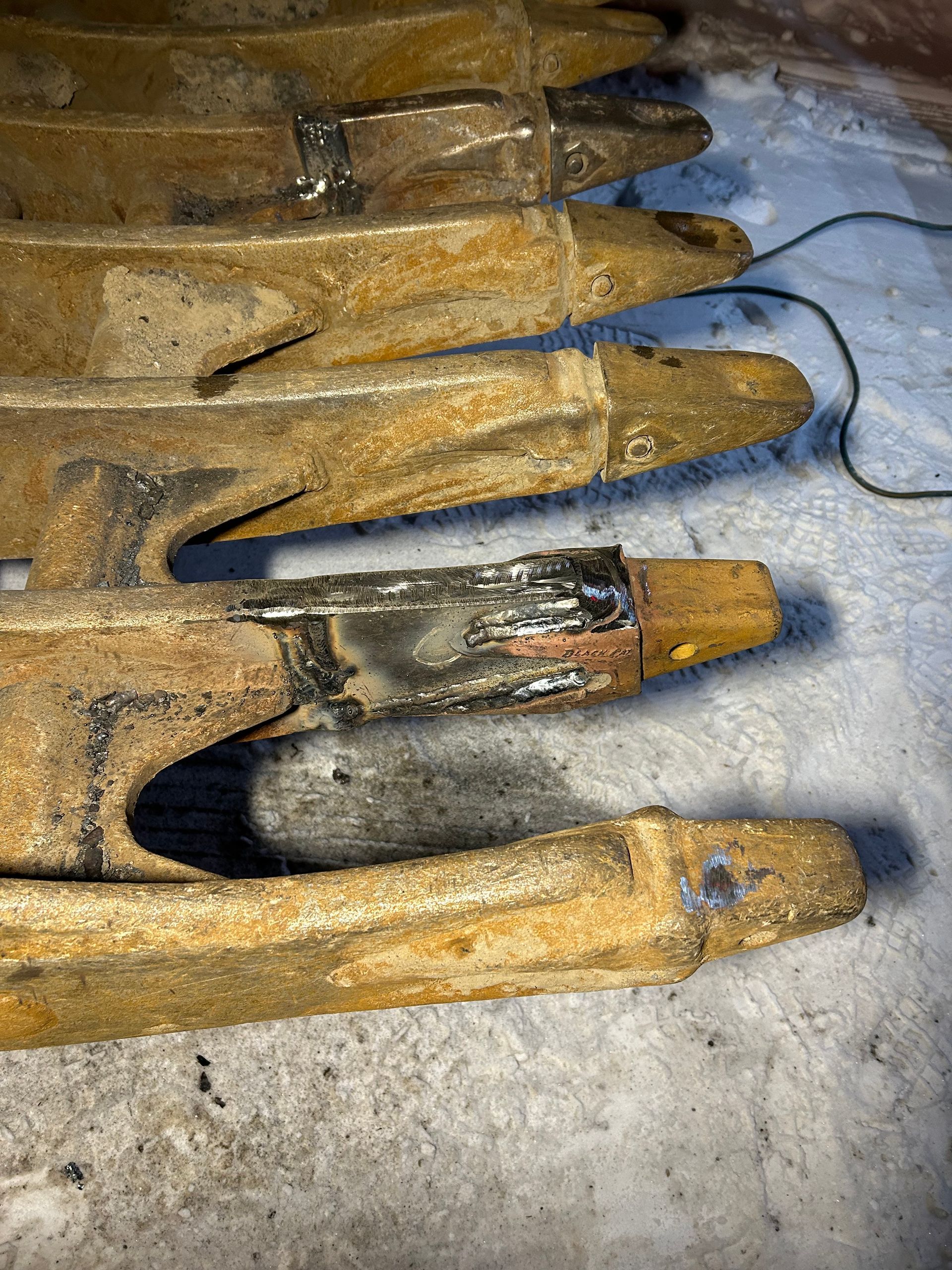 Gros plan sur plusieurs lames de charrue en métal rouillé, probablement destinées à une machine agricole, posées sur une surface.