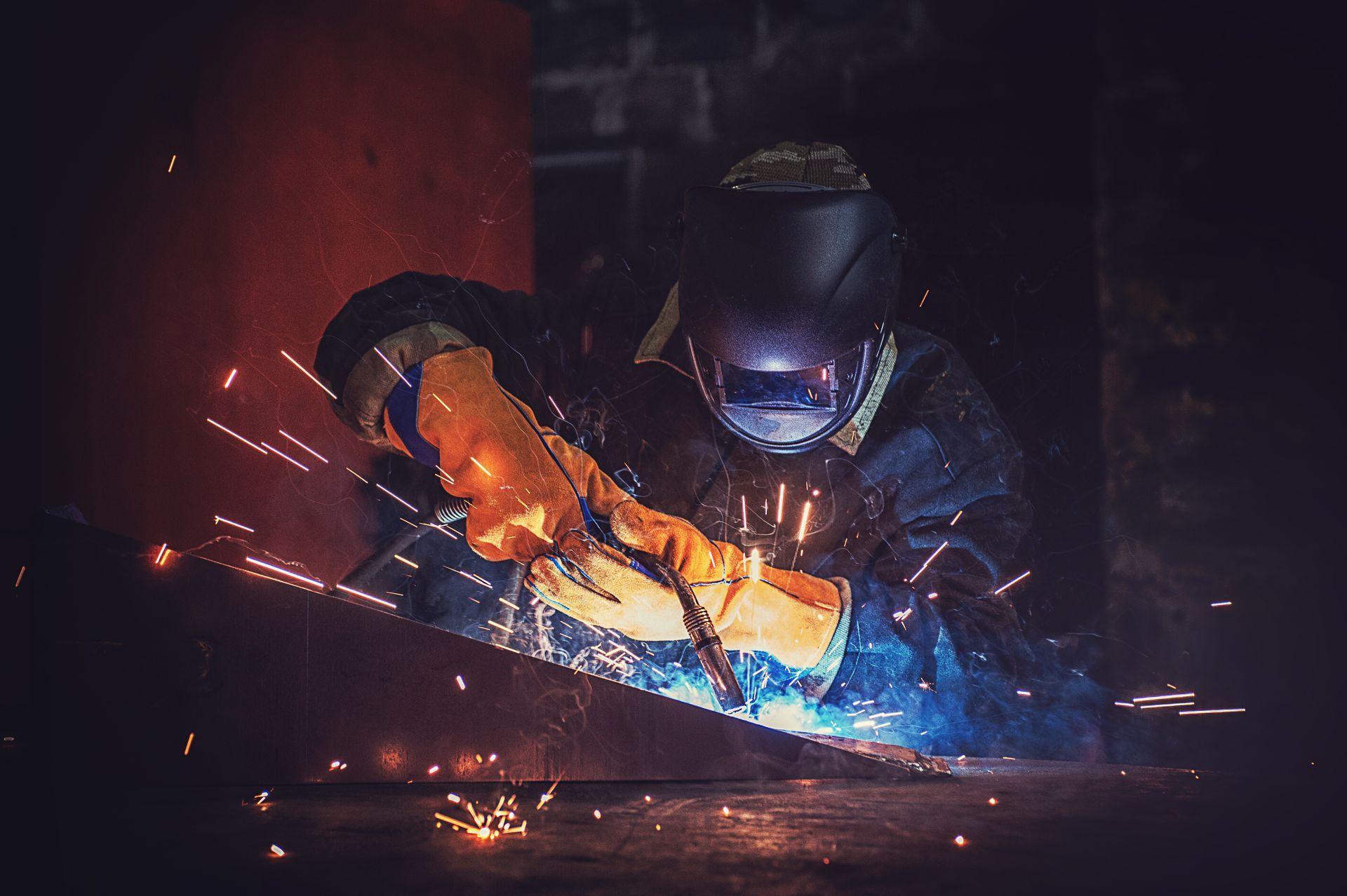 Un soudeur portant un équipement de protection soude du métal en produisant des étincelles vives dans un atelier faiblement éclairé.
