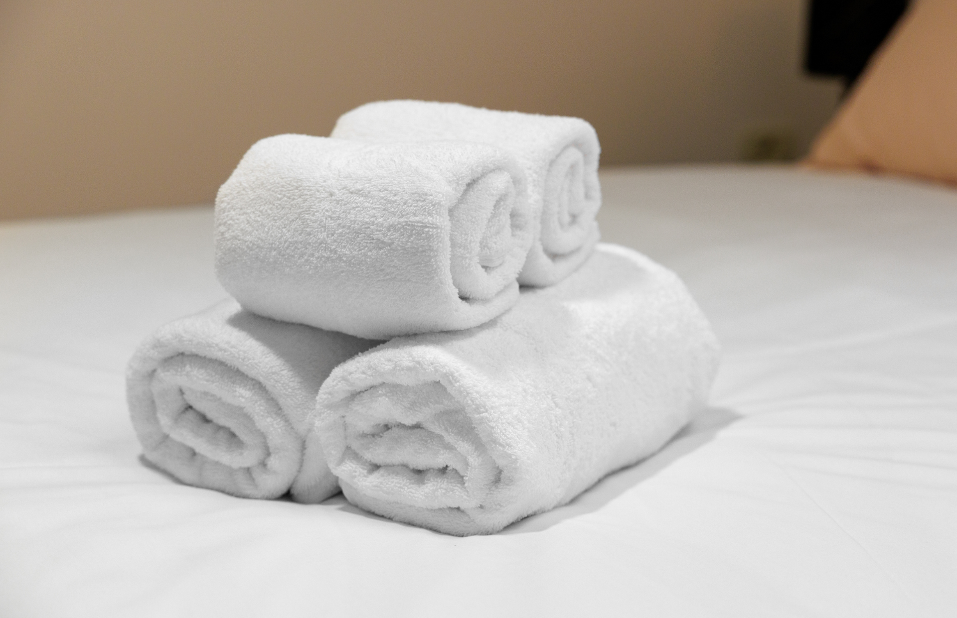 Rolled white towels stacked on a neatly made bed