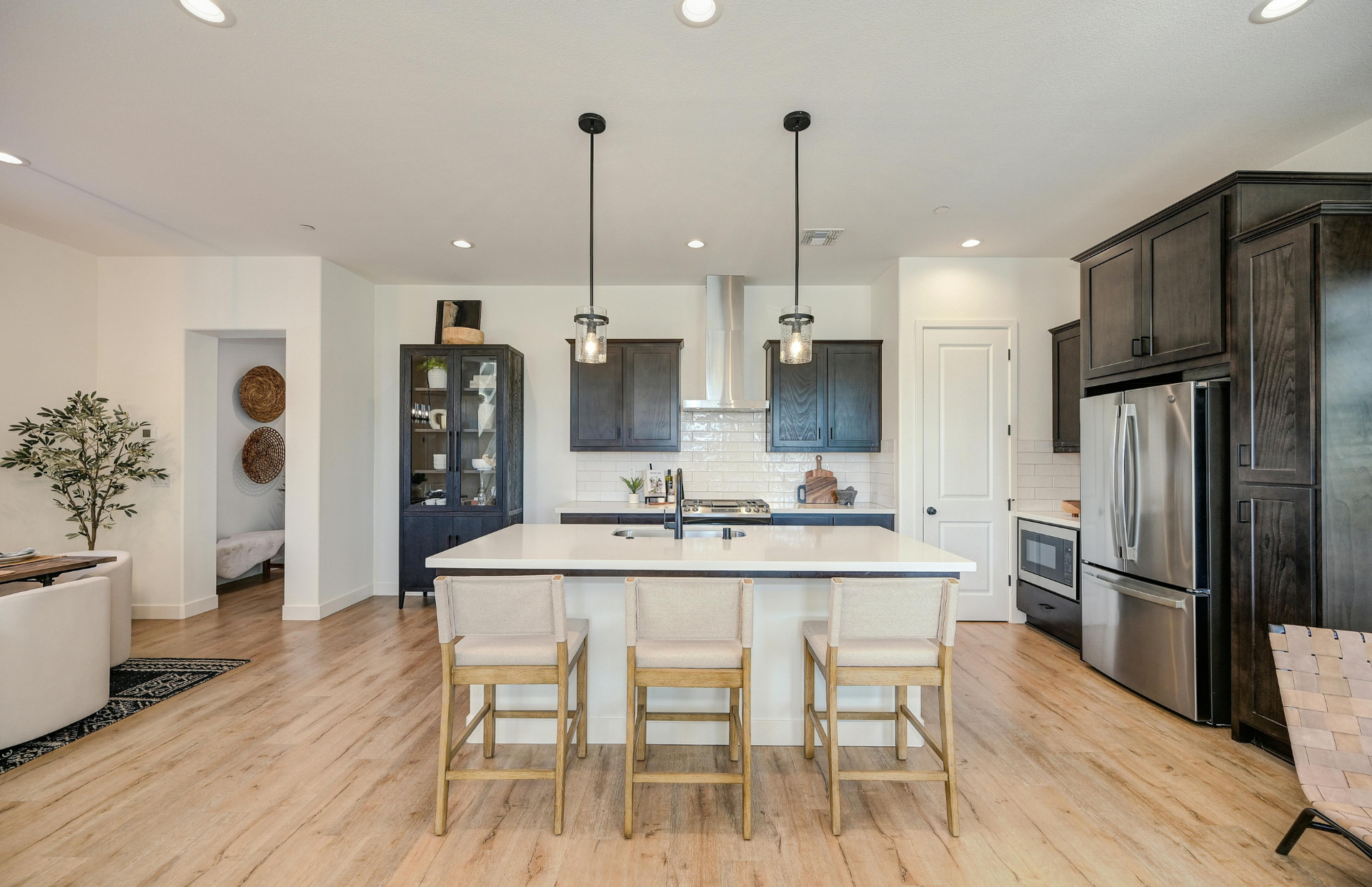 Bright modern kitchen with white island, pendant lights, wood floors, and dark cabinets