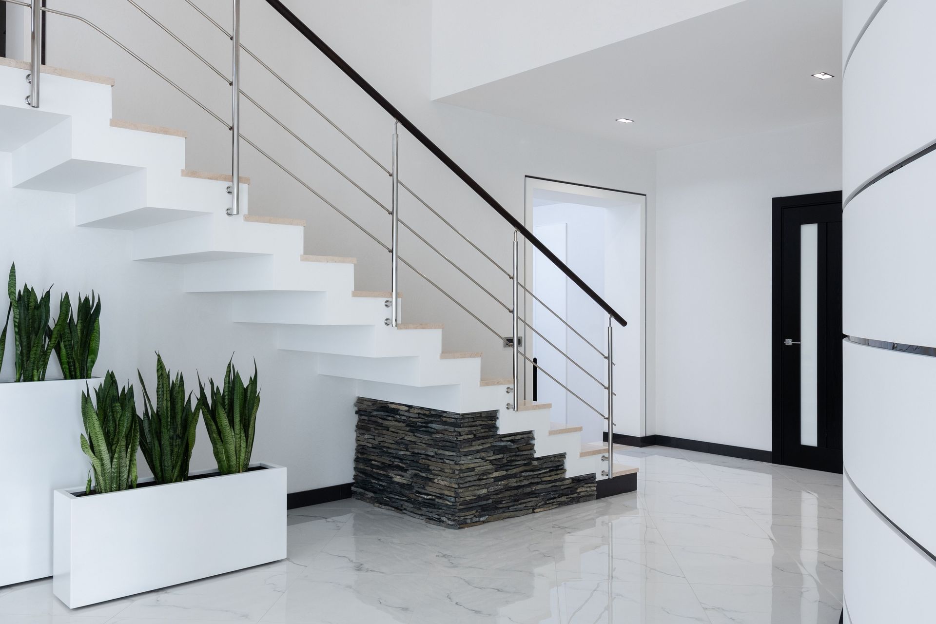 Modern open-plan office with desks, black chairs, large windows, and bright natural light