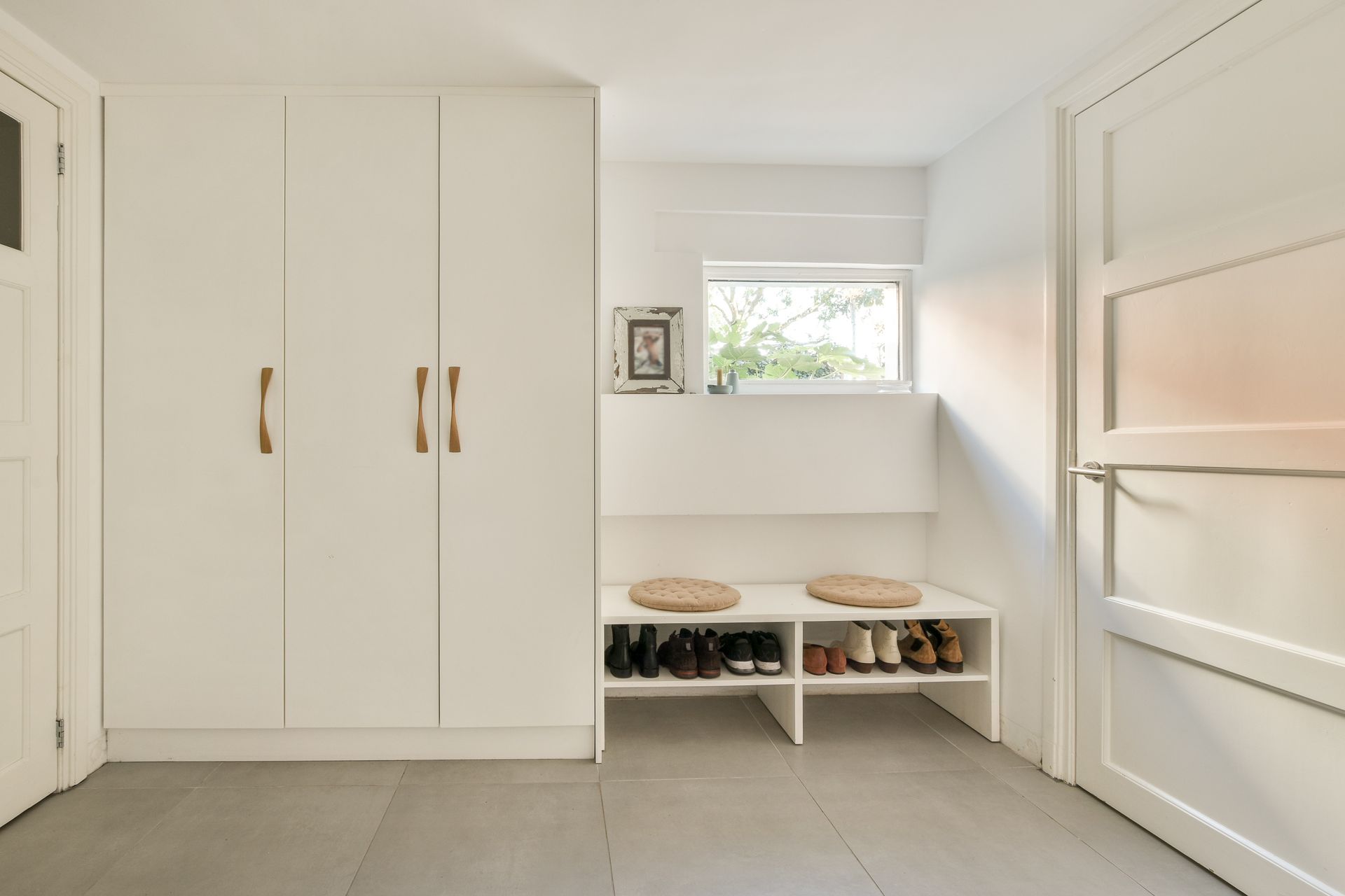 Bright white mudroom with built-in cabinets, bench seating, and wall shelves on a tiled floor.