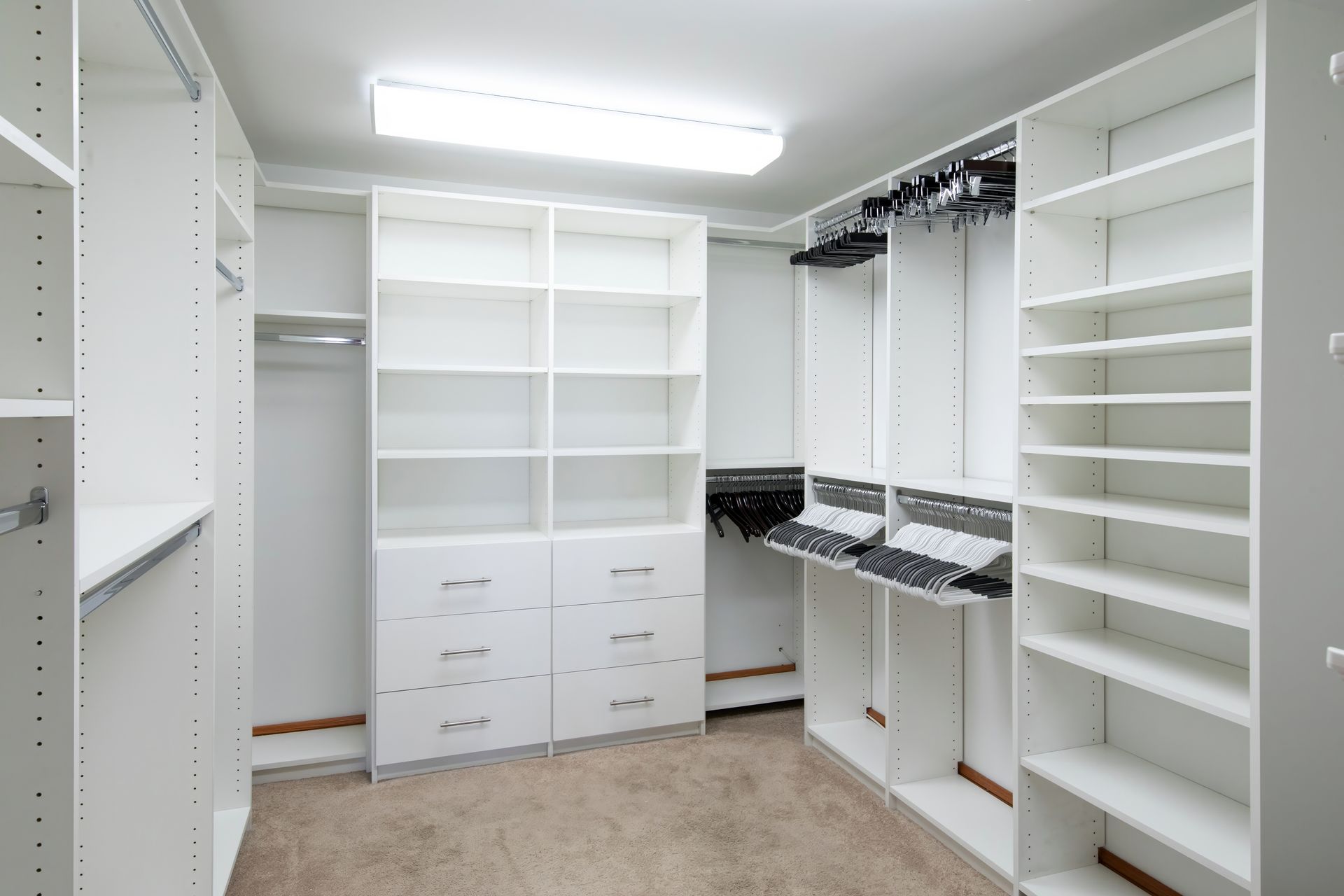 Walk-in closet with white shelving, drawers, and hanging rods under a ceiling light.