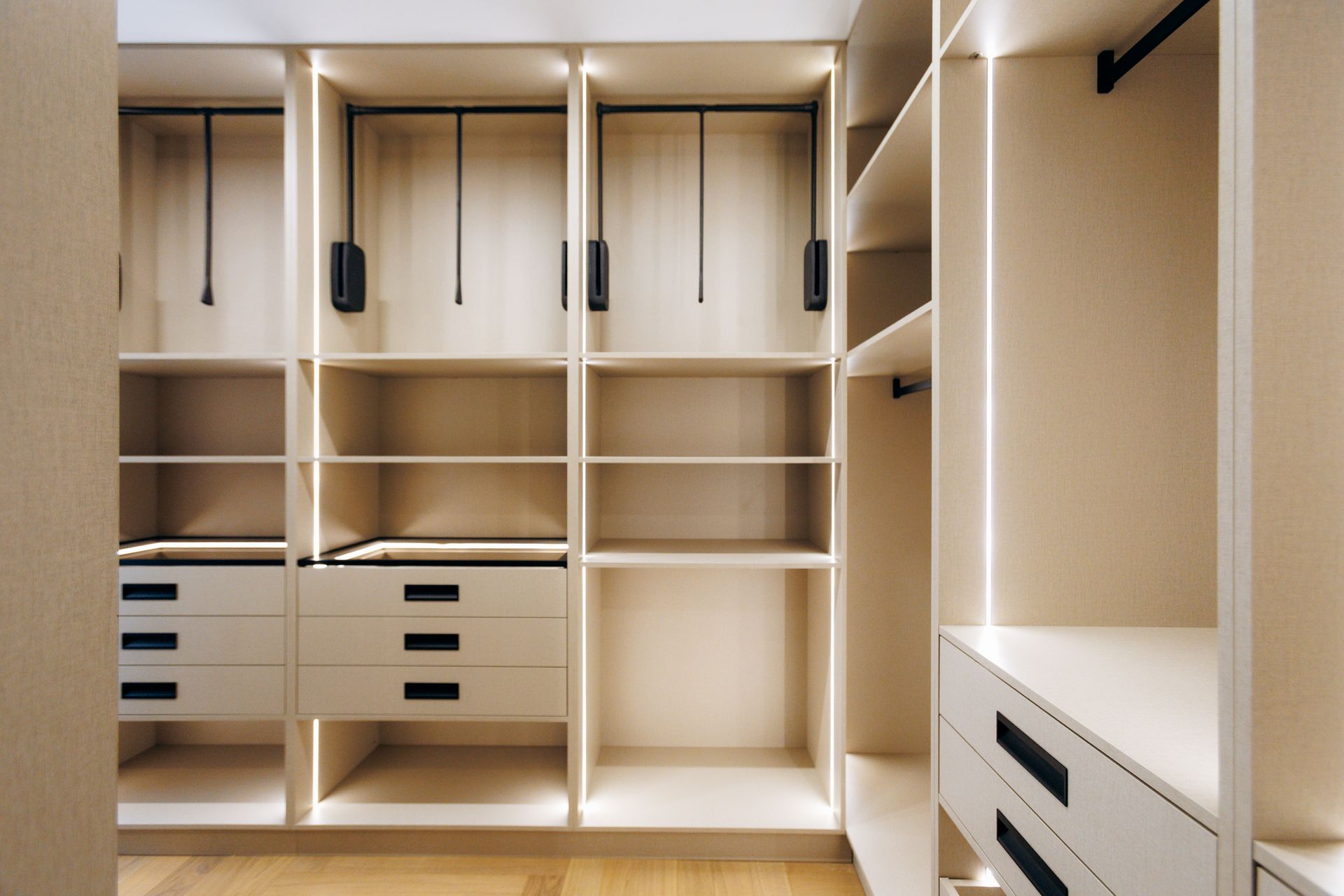 Empty walk-in closet with beige shelves, drawers, and hanging rods under recessed lighting Empty walk-in closet with beige shelves, drawers, and hanging rods under recessed lighting