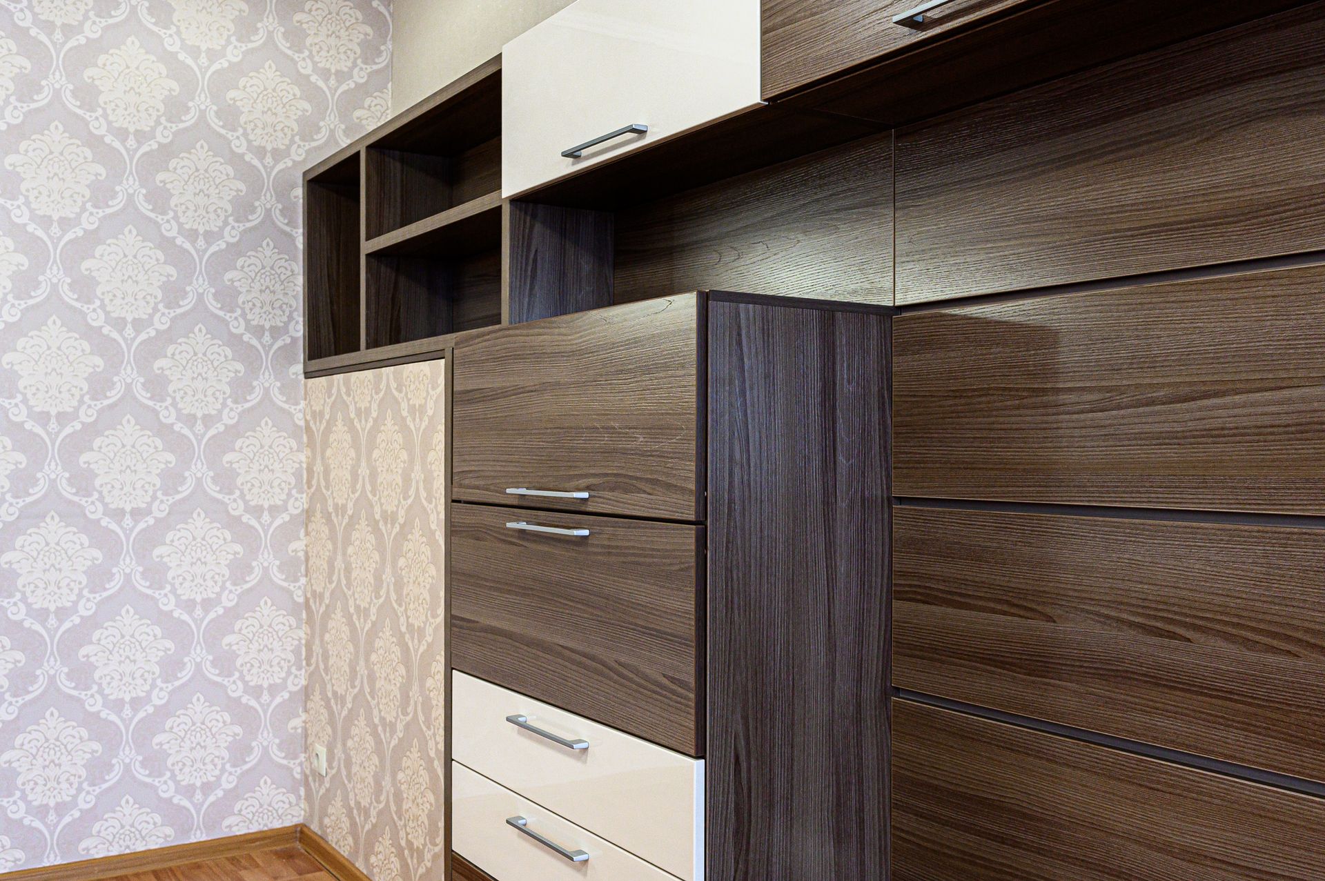 Wooden built-in wardrobe with drawers and shelves against patterned wallpaper in a room