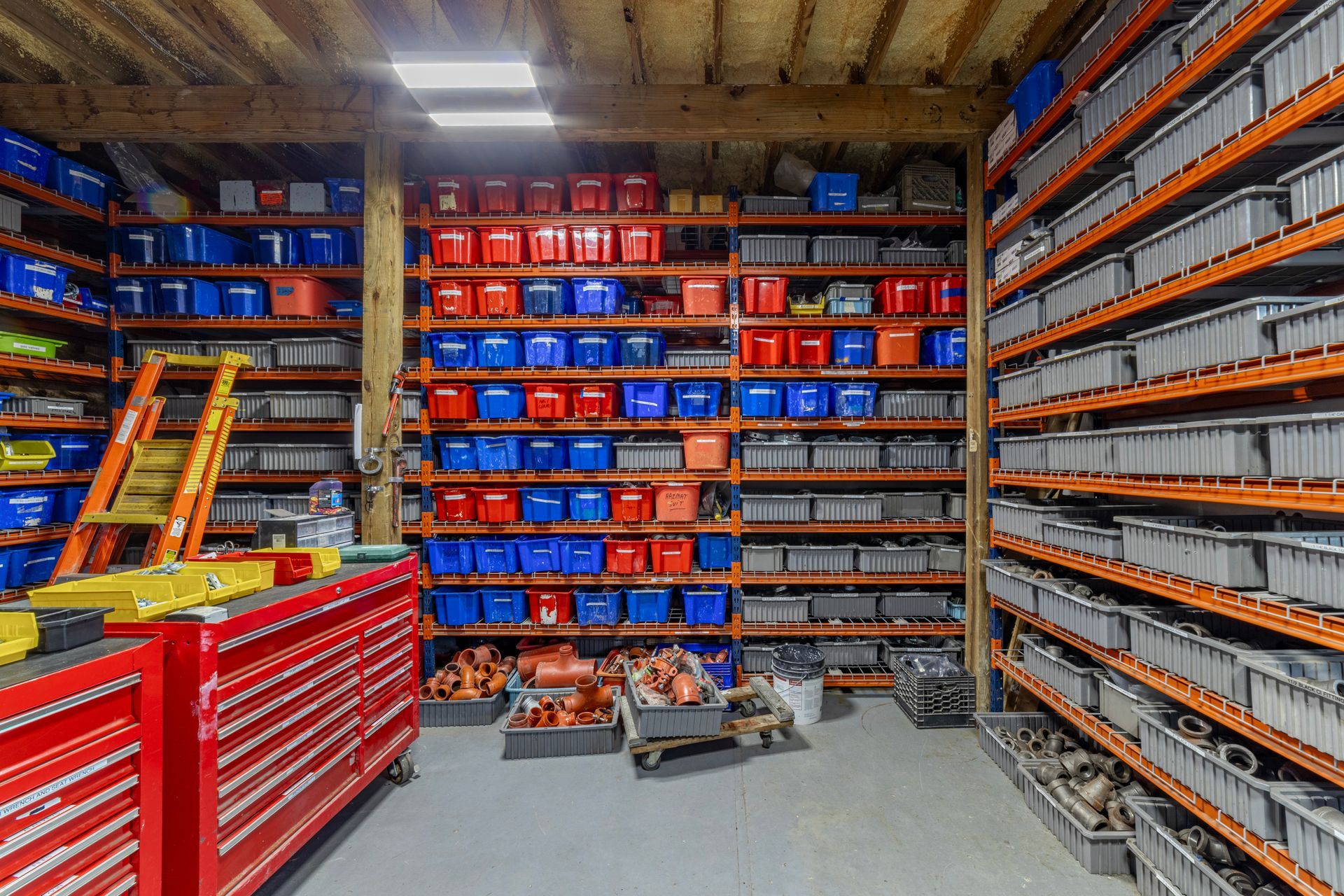 Storage warehouse aisle with red tool chests, shelves of blue and orange bins, and stacked parts. Storage warehouse aisle with red tool chests, shelves of blue and orange bins, and stacked parts.