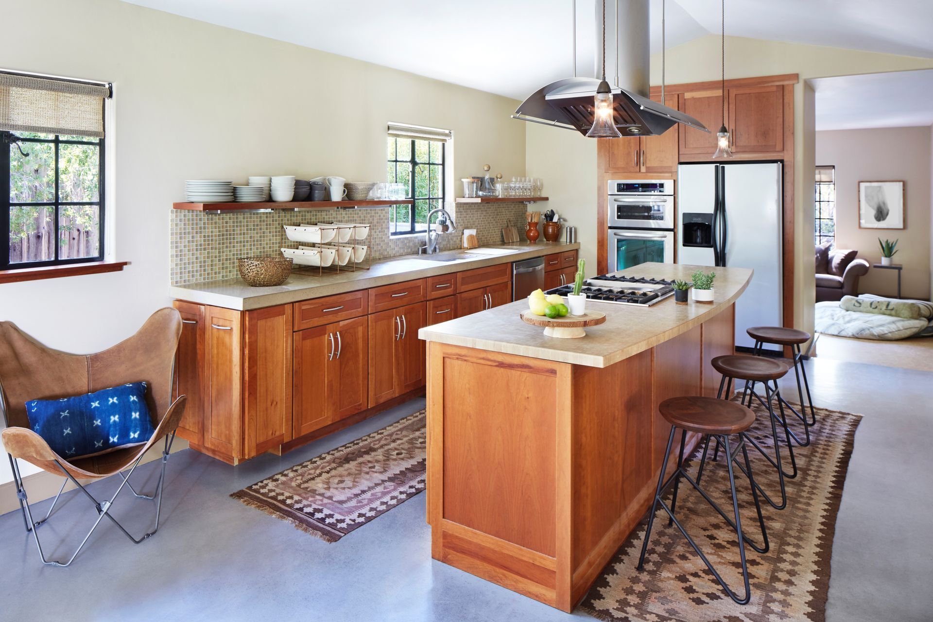 Warm kitchen interior with wood cabinets, island, stools, rugs, and a blue folding chair by the window Warm kitchen interior with wood cabinets, island, stools, rugs, and a blue folding chair by the window