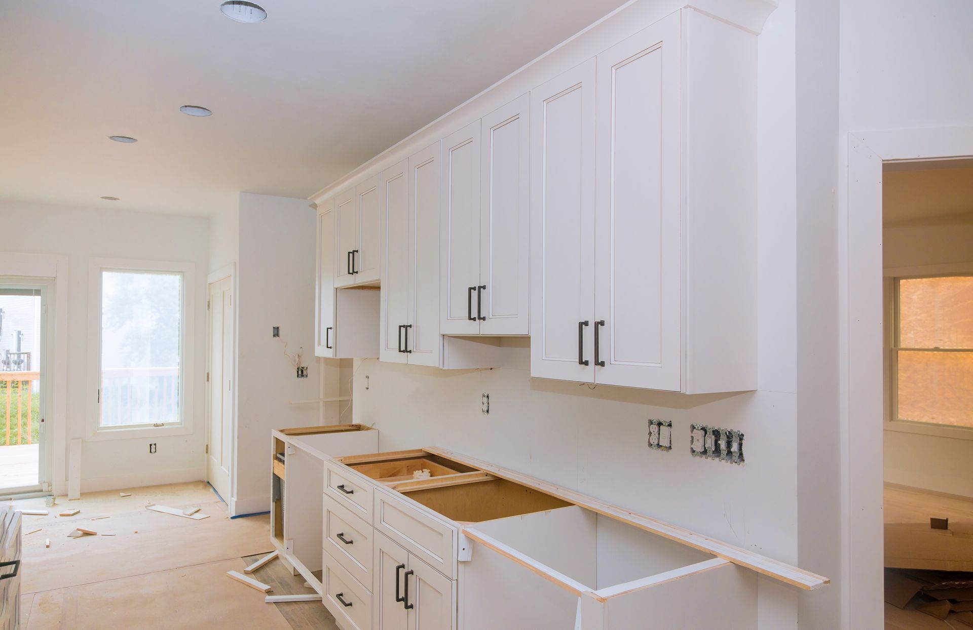 Bright white kitchen under renovation with unfinished cabinets, countertops, and flooring. Bright white kitchen under renovation with unfinished cabinets, countertops, and flooring.