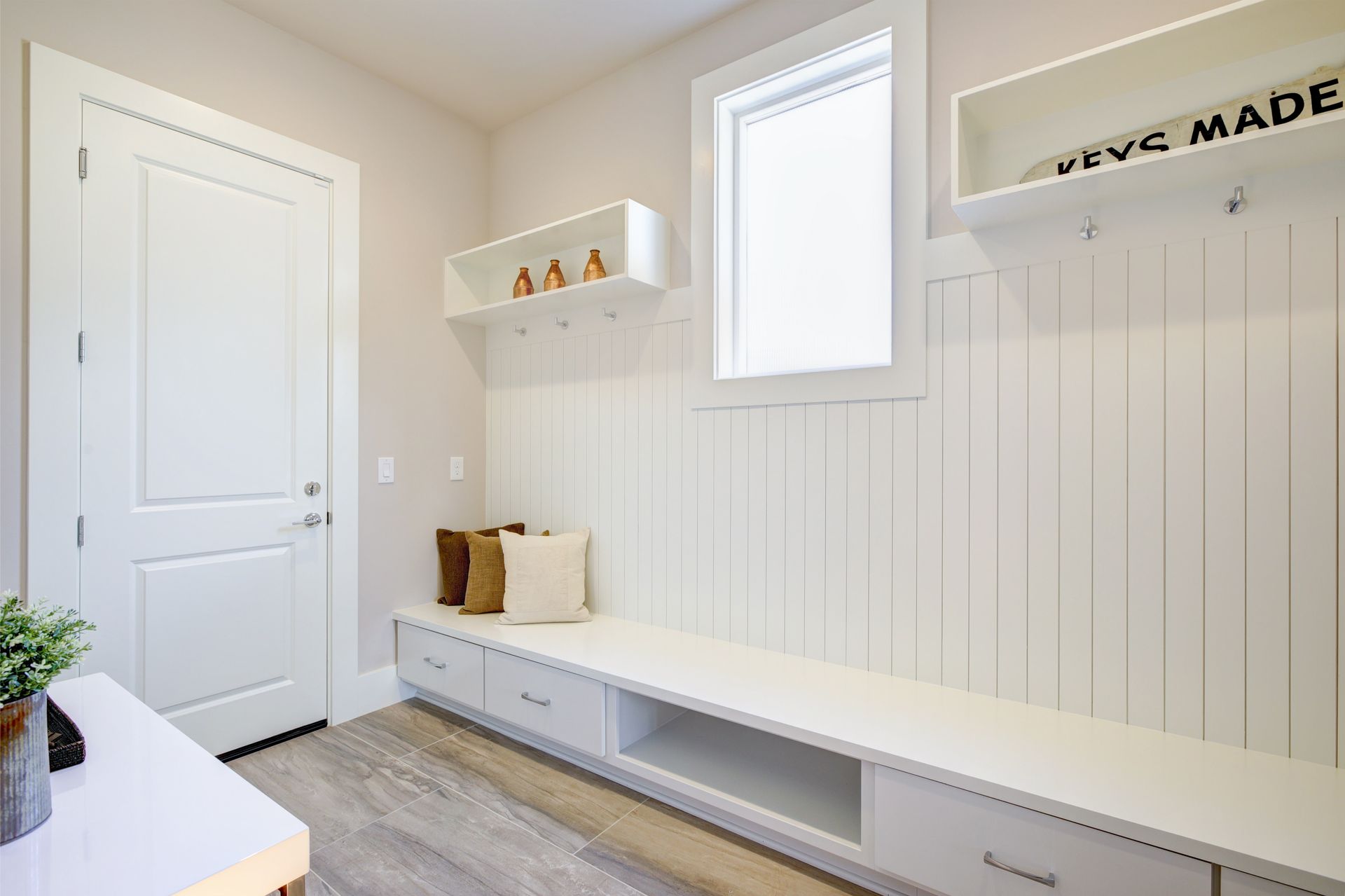 Bright mudroom with white bench, hooks, small window, and light wood floor Bright mudroom with white bench, hooks, small window, and light wood floor