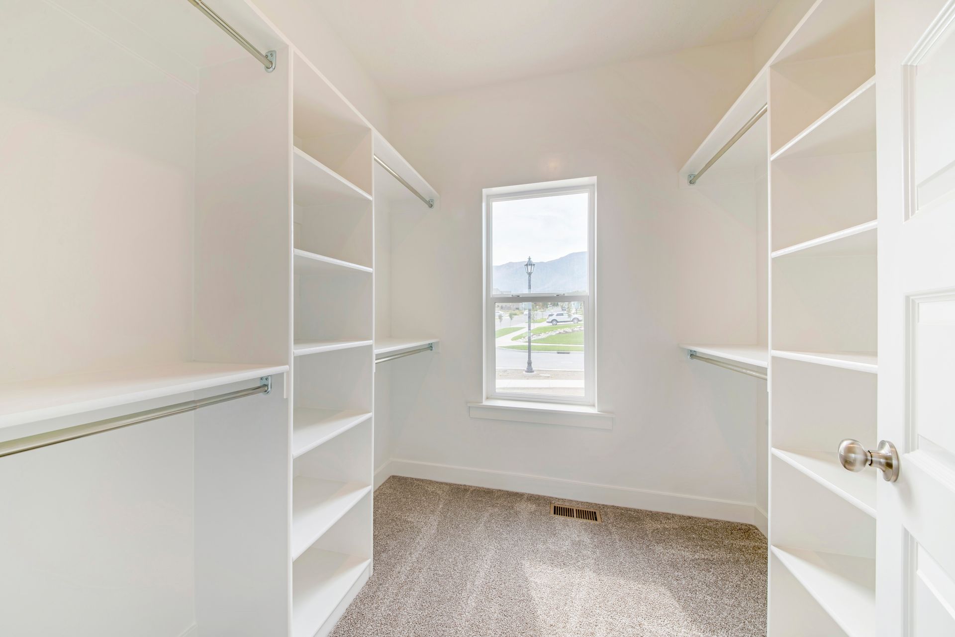 Warm kitchen interior with wood cabinets, island, stools, rugs, and a blue folding chair by the window Walk-in closet with white shelving and carpet, window at the end.