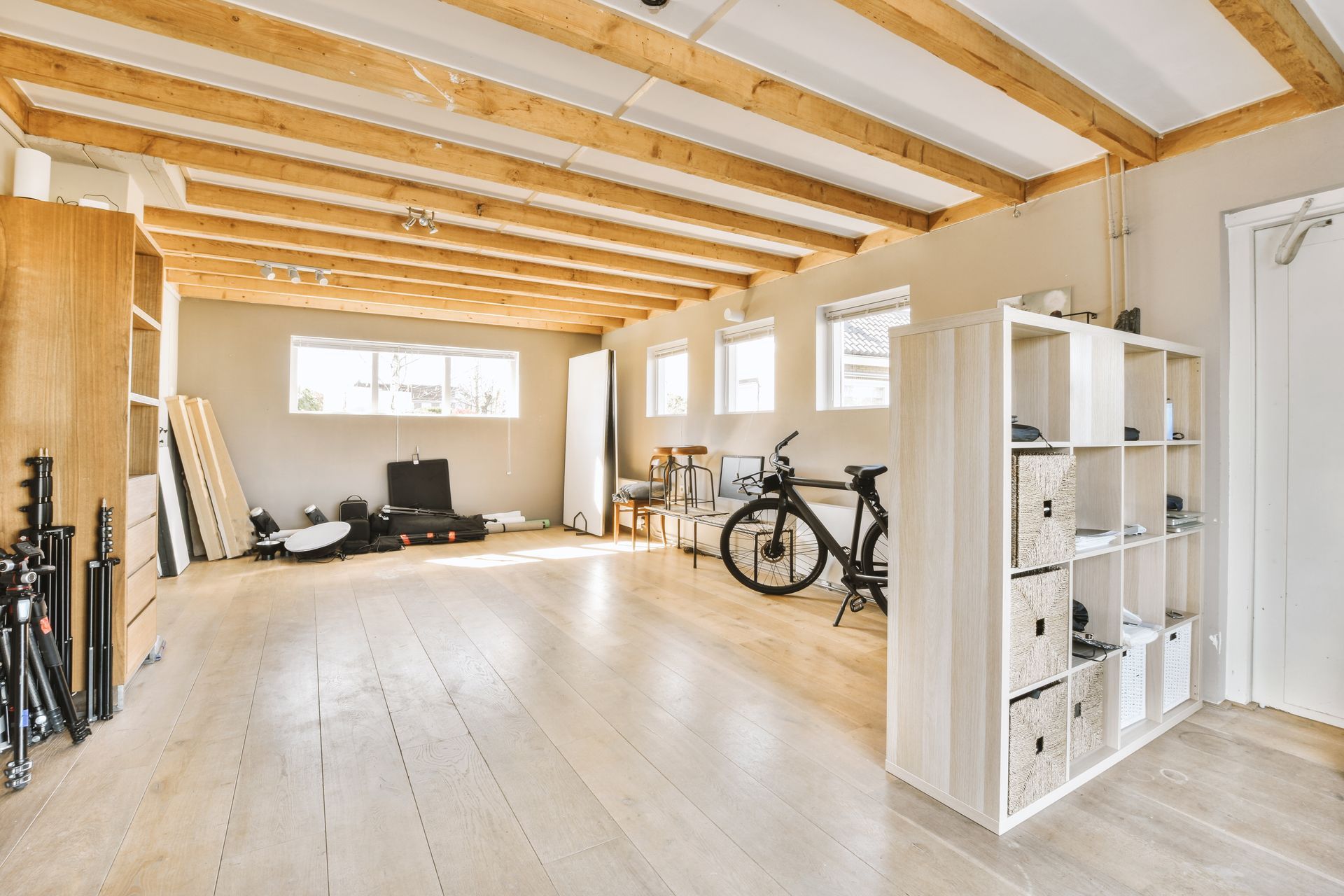 Bright, unfinished loft room with exposed beams, bikes, shelving, and large windows Bright, unfinished loft room with exposed beams, bikes, shelving, and large windows