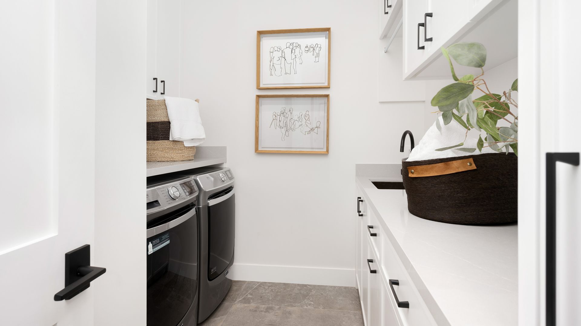 Narrow laundry room with a washer, dryer, white cabinets, and wall art. Narrow laundry room with a washer, dryer, white cabinets, and wall art.