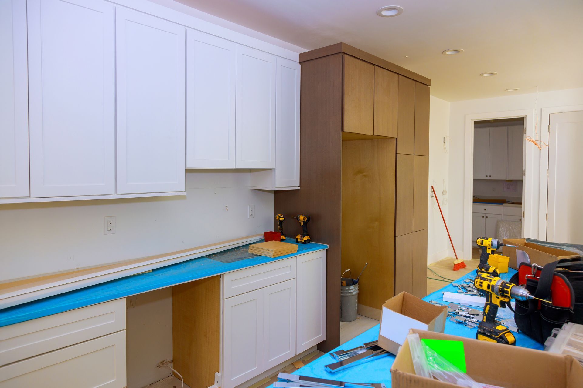 Partially renovated kitchen with white cabinets, wood pantry, tools, and materials scattered on counters and floor Partially renovated kitchen with white cabinets, wood pantry, tools, and materials scattered on counters and floor