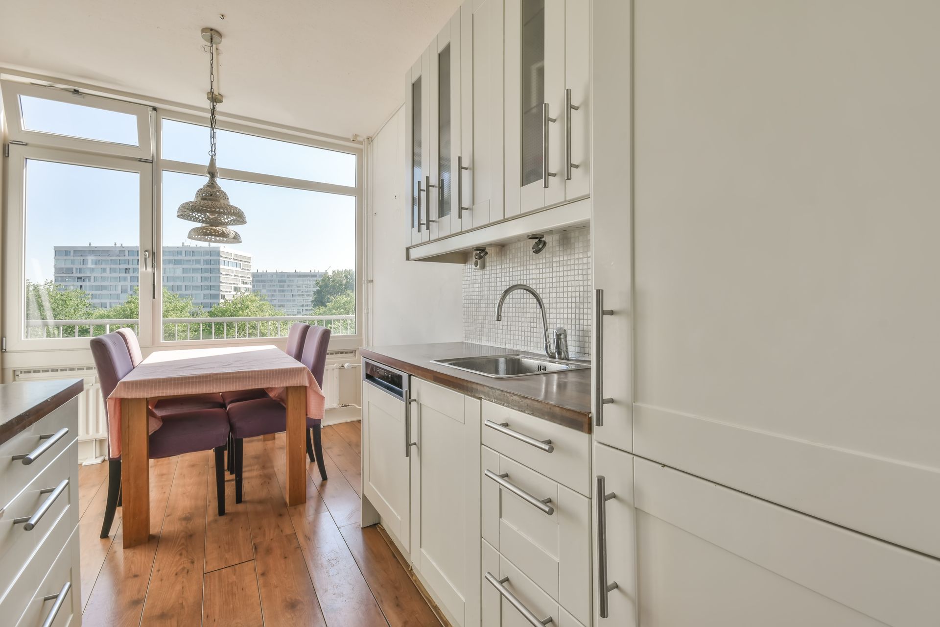 Bright kitchen with a wooden dining table by large windows and white cabinets overlooking greenery