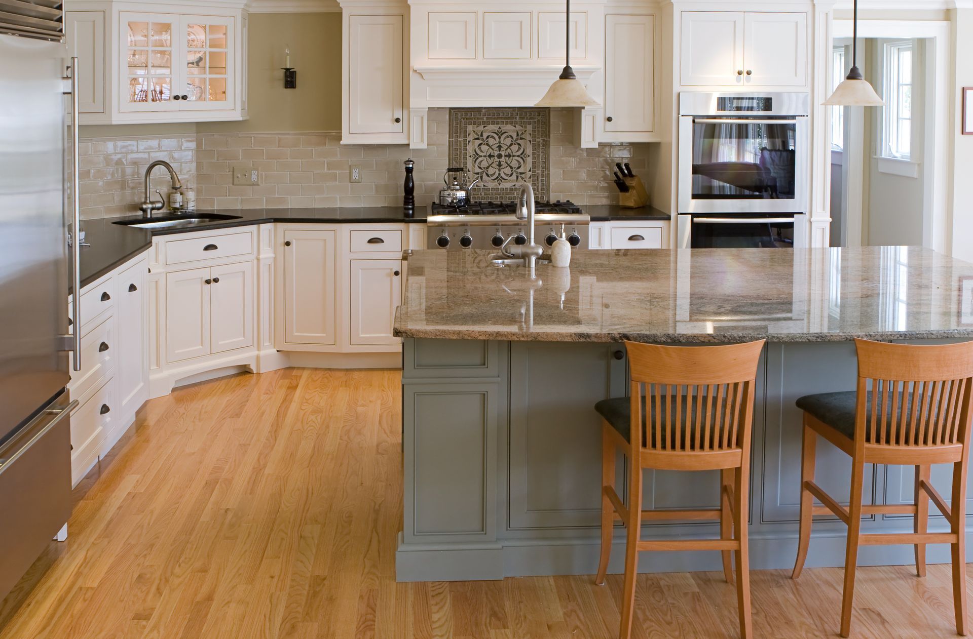 Bright modern kitchen with granite island, white cabinets, and two wooden bar stools