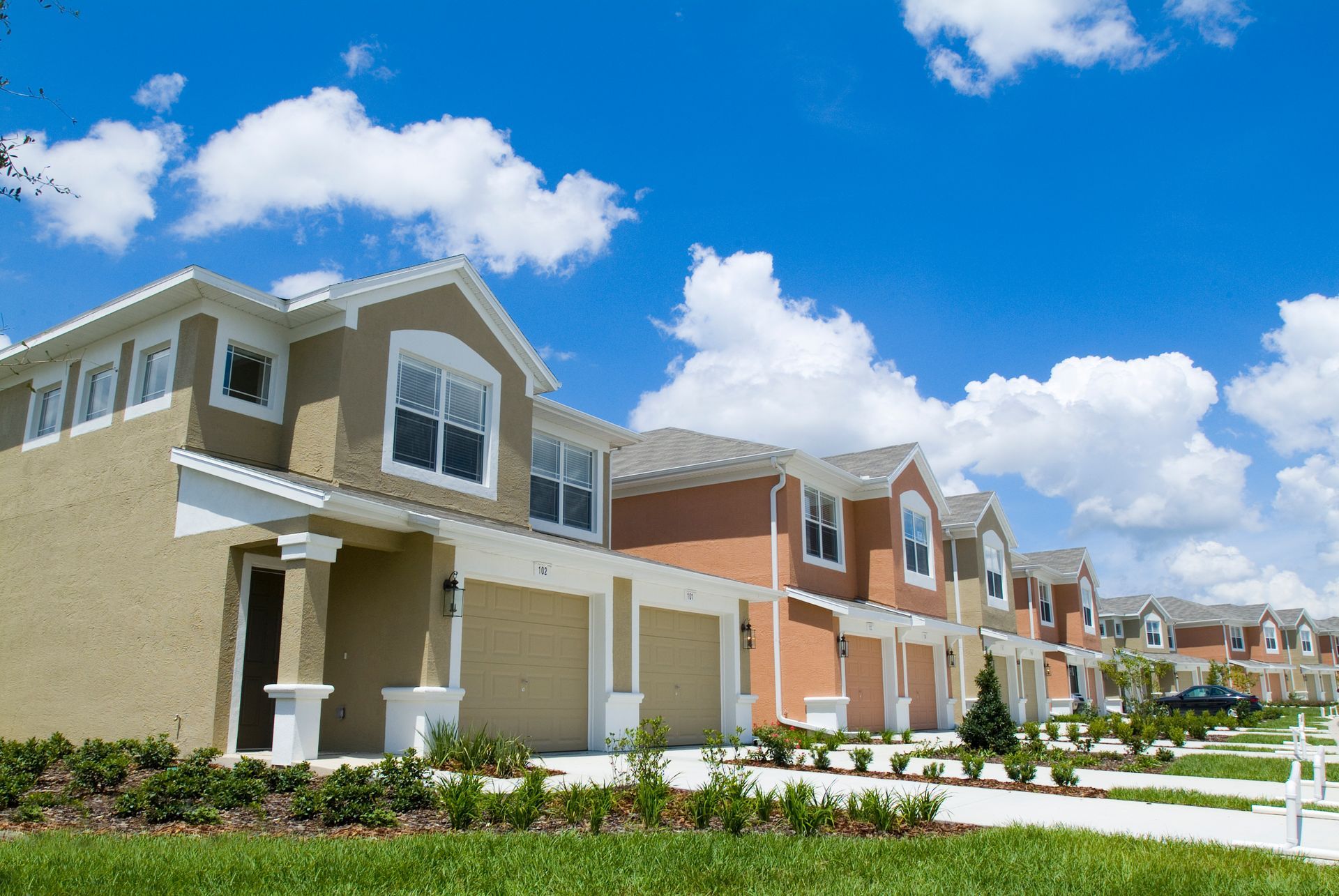 Row of modern suburban townhouses with garages under a bright blue sky and clouds